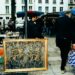 A smiling artist arranges colorful paintings at a New York City street fair booth