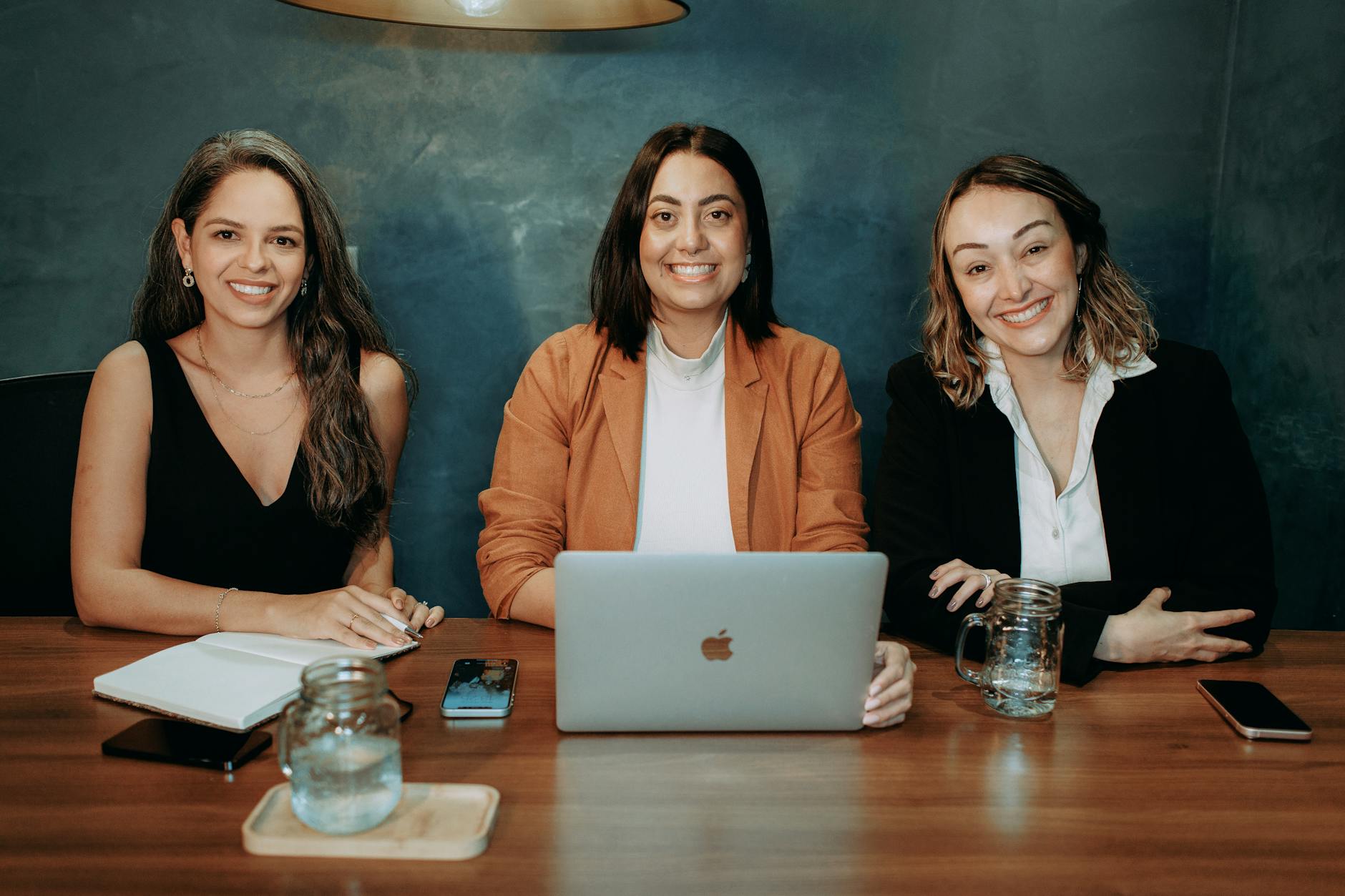 Three entrepreneurs discuss NYC business growth strategy at a Manhattan office table with a laptop open to financial data.