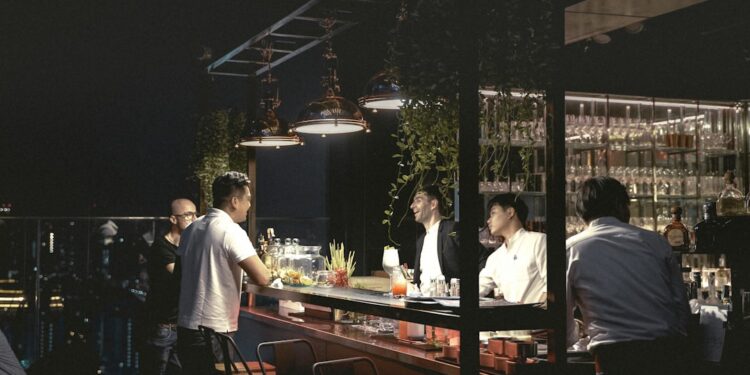 A man enjoying a craft cocktail at one of the best rooftop bars in NYC with the Manhattan skyline glowing behind her at dusk