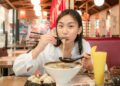 A woman carefully lifts a soup dumpling with chopsticks at a table in Flushing Chinatown, New York