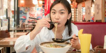 A woman carefully lifts a soup dumpling with chopsticks at a table in Flushing Chinatown, New York