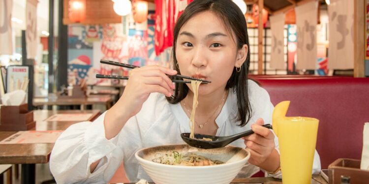 A woman carefully lifts a soup dumpling with chopsticks at a table in Flushing Chinatown, New York