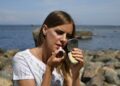 woman-in-makeup-application-mirror-unsplash - NYCwebzine A woman applying primer to her face in preparation for a summer makeup routine in New York City