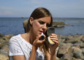A woman applying primer to her face in preparation for a summer makeup routine in New York City