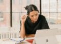 A woman reviews co-op purchase documents at a Brooklyn kitchen table, comparing monthly costs of a Brooklyn co-op.