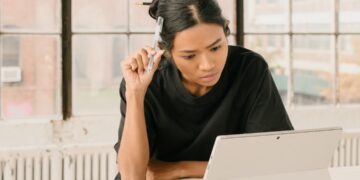 A woman reviews co-op purchase documents at a Brooklyn kitchen table, comparing monthly costs of a Brooklyn co-op.