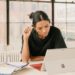 woman-reviewing-apartment-documents-brooklyn-unsplash - NYCwebzine Une femme examine les documents d'achat de co-op à une table de cuisine à Brooklyn, comparant les coûts mensuels d'une co-op à Brooklyn.