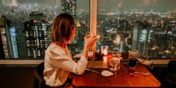A woman enjoying rooftop dining in NYC with the Manhattan skyline glowing behind her at sunset
