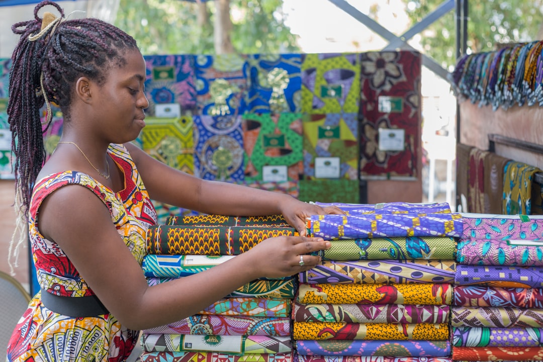 A woman arranges colorful West African fabric bolts at an outdoor market stall in the Bronx, reflecting the vibrant culture