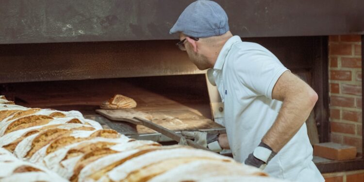 bakery-owner-serving-gluten-free-bread-unsplash - NYCwebzine A baker hands a gluten-free loaf to a customer inside a Manhattan bakery, showing the growing demand for gluten-free.