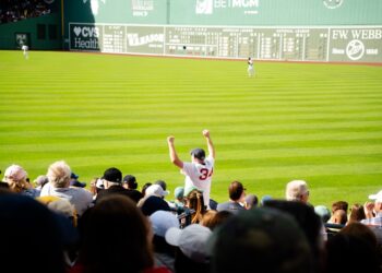 A smiling fan cheering in the upper deck while watching a baseball tickets game on a sunny summer afternoon