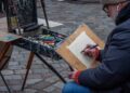 A man sits outdoors with a sketchbook, taking part in free art classes in a New York City park setting