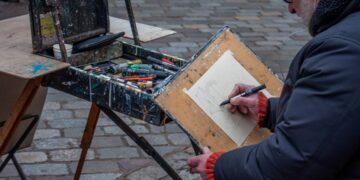 A man sits outdoors with a sketchbook, taking part in free art classes in a New York City park setting