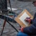 A man sits outdoors with a sketchbook, taking part in free art classes in a New York City park setting
