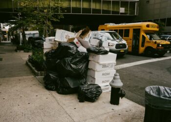 overflowing garbage bags and cardboard boxes piled on New York City sidewalk at night beside a fire hydrant.