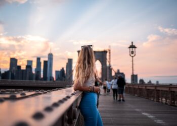 photographer-woman-brooklyn-bridge-sunrise-unsplash - NYCwebzine A woman frames the Brooklyn Bridge in warm morning light, a classic outdoor photography spot in NYC