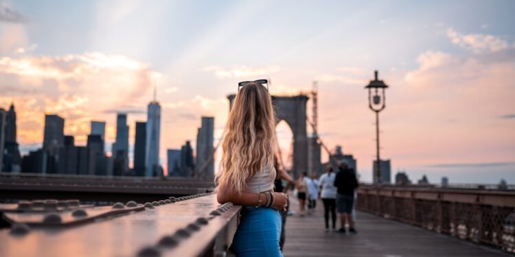 A woman frames the Brooklyn Bridge in warm morning light, a classic outdoor photography spot in NYC
