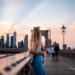 photographer-woman-brooklyn-bridge-sunrise-unsplash - NYCwebzine A woman frames the Brooklyn Bridge in warm morning light, a classic outdoor photography spot in NYC