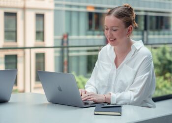 A professional woman works at a laptop inside one of New York City's best co-working spaces, with modern open-plan desks.