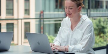A professional woman works at a laptop inside one of New York City's best co-working spaces, with modern open-plan desks.