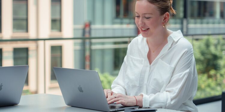 professional-woman-laptop-open-coworking-unsplash - NYCwebzine A professional woman works at a laptop inside one of New York City's best co-working spaces, with modern open-plan desks.