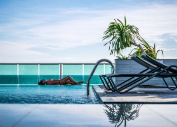 A woman resting by one of Manhattan's rooftop pools on a sun-drenched terrace with city skyline views behind her