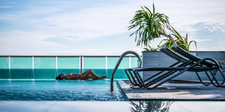 rooftop-pool-relaxation-unsplash - NYCwebzine A woman resting by one of Manhattan's rooftop pools on a sun-drenched terrace with city skyline views behind her