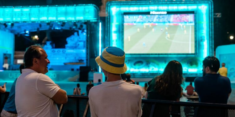 soccer-fans-cheering-big-screen-outdoor-unsplash - NYCwebzine A crowd of fans cheering at one of the FIFA World Cup fan zones on a large outdoor screen in New York City