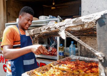A West African man serves a bowl of fufu and soup at a busy Bronx restaurant, representing the heart of the West African food
