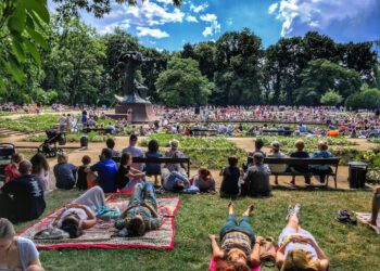 A diverse crowd of people enjoying free outdoor concerts in a New York City park on a summer evening