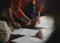 entrepreneur-signing-business-documents-desk-unsplash - NYCwebzine A focused entrepreneur completes paperwork to register a sole proprietorship at a city office desk in New York