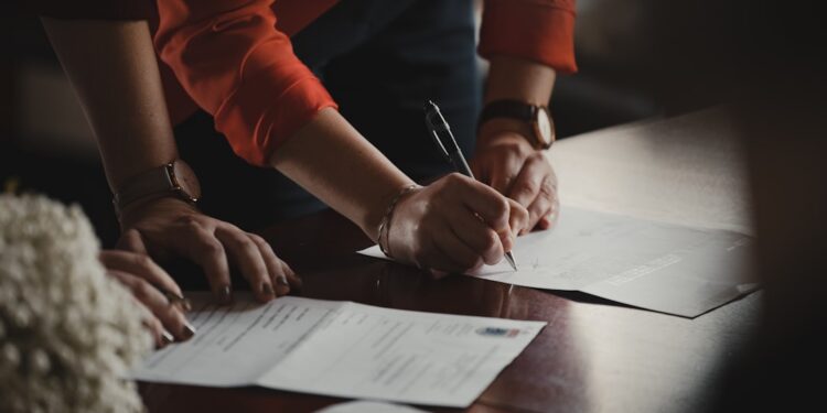 entrepreneur-signing-business-documents-desk-unsplash - NYCwebzine A focused entrepreneur completes paperwork to register a sole proprietorship at a city office desk in New York