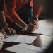 entrepreneur-signing-business-documents-desk-unsplash - NYCwebzine A focused entrepreneur completes paperwork to register a sole proprietorship at a city office desk in New York