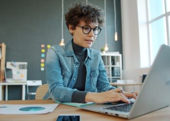 A freelancer pauses at her desk to manage burnout by stepping back from her screen and breathing