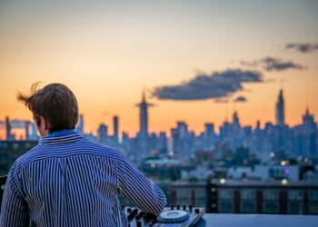 A man enjoying a cocktail on a Manhattan rooftop terrace at the city's top private clubs with a skyline view behind him