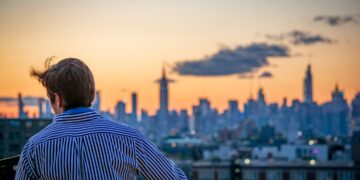 man-rooftop-skyline-cocktail-unsplash - NYCwebzine A man enjoying a cocktail on a Manhattan rooftop terrace at the city's top private clubs with a skyline view behind him