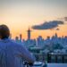 man-rooftop-skyline-cocktail-unsplash - NYCwebzine A man enjoying a cocktail on a Manhattan rooftop terrace at the city's top private clubs with a skyline view behind him