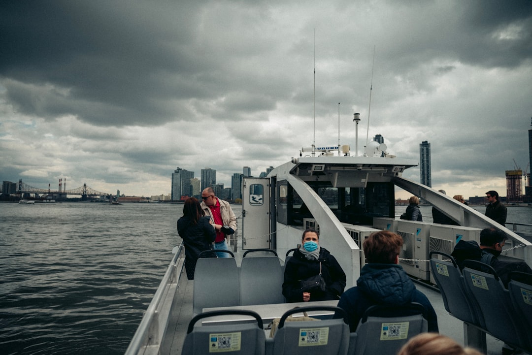 A group of tourists boarding an NYC Ferry at a waterfront landing with the city skyline behind them