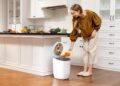 woman-kitchen-compost-bin-unsplash - NYCwebzine A woman placing food scraps into a countertop bin as part of her daily composting routine in a New York City kitchen.