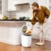 woman-kitchen-compost-bin-unsplash - NYCwebzine A woman placing food scraps into a countertop bin as part of her daily composting routine in a New York City kitchen.