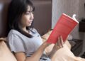 woman-reading-book-in-bed-unsplash - NYCwebzine A woman sitting up in bed with a lamp and herbal tea, practicing a calm wind-down routine in her apartment