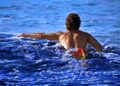 swimmer-entering-ocean-unsplash - NYCwebzine A swimmer wading into the open water at Brighton Beach, representing the open-water culture of a New York City swimming club