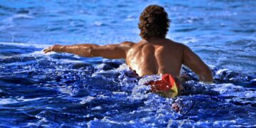 swimmer-entering-ocean-unsplash - NYCwebzine A swimmer wading into the open water at Brighton Beach, representing the open-water culture of a New York City swimming club