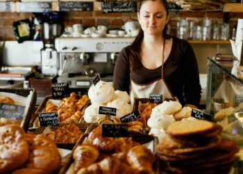 A woman carefully selecting a pastry at a gluten-free bakeries counter in New York City, surrounded by baked goods.