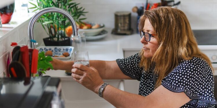 woman-organizing-glass-jars-kitchen-unsplash - NYCwebzine A woman arranging labeled glass jars on an open shelf as part of building a lower-waste kitchen in a New York City apartment