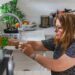 woman-organizing-glass-jars-kitchen-unsplash - NYCwebzine A woman arranging labeled glass jars on an open shelf as part of building a lower-waste kitchen in a New York City apartment