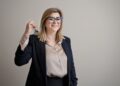woman-signing-apartment-lease-with-keys-unsplash - NYCwebzine An NYC renter reviews a lease document at a table with a real estate agent in a Manhattan apartment
