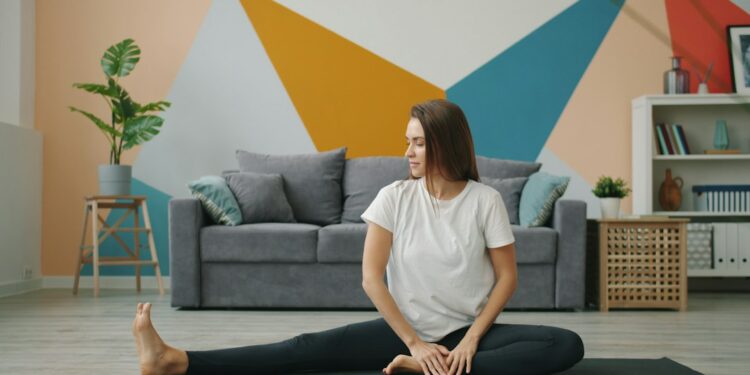 woman-stretching-home-unsplash - NYCwebzine A woman practicing a recovery routine on a yoga mat in a compact New York City apartment, surrounded by soft morning light