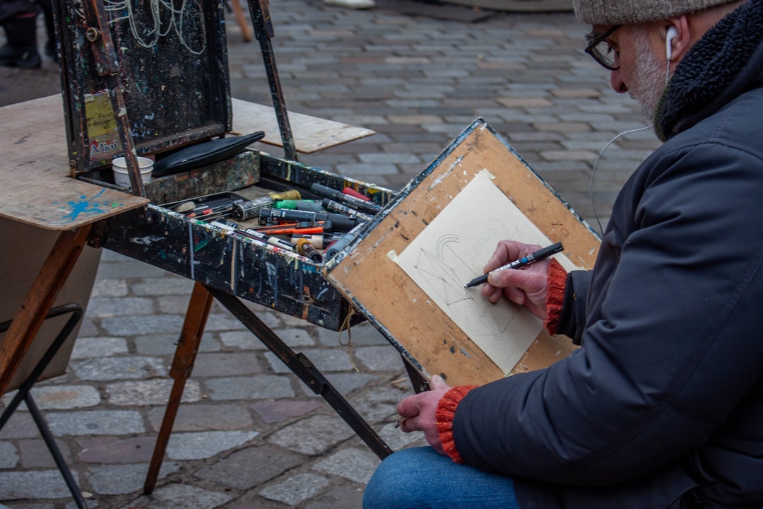 A man sits outdoors with a sketchbook, taking part in free art classes in a New York City park setting